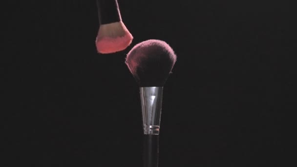Две щетки для макияжа с розовым порошком на черном фоне — стоковое видео