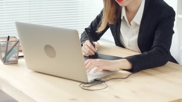 Молодая женщина графический дизайнер работает на ноутбуке с помощью планшета в современном офисе — стоковое видео