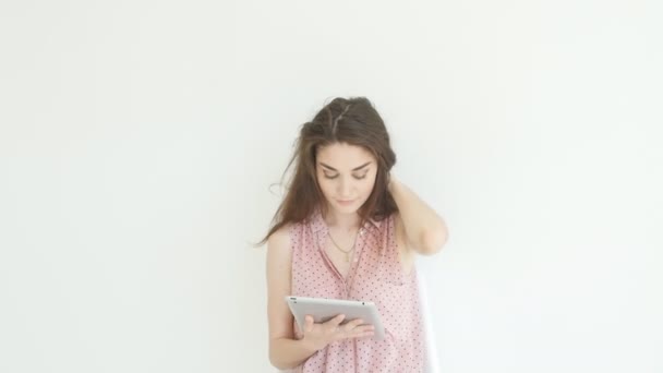 Eletrônica e conceito de gadgets pessoais. Jovem mulher lendo informações sobre seu computador tablet no interior branco — Vídeo de Stock