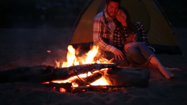 友情、愛、関係の概念。夜のビーチでキャンプファイヤーで座っている若い幸せなカップル — ストック動画