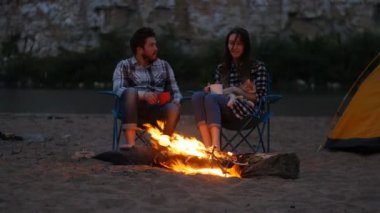 Dostluk, sevgi ve ilişkiler kavramı. Plaj, gece kamp ateşi ile genç mutlu oturan çift