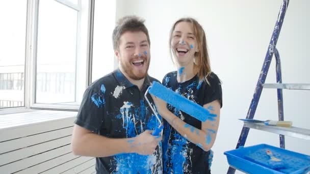 Молодая счастливая пара веселится во время ремонта и покраски своей квартиры — стоковое видео