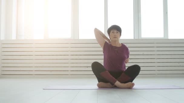 Concepto de armonía, deporte y salud. Mujer de mediana edad haciendo yoga en un interior blanco — Vídeos de Stock