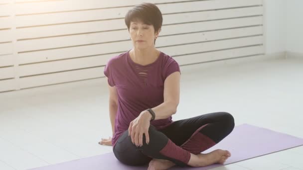 Concepto de armonía, deporte y salud. Mujer de mediana edad haciendo yoga en un interior blanco — Vídeos de Stock