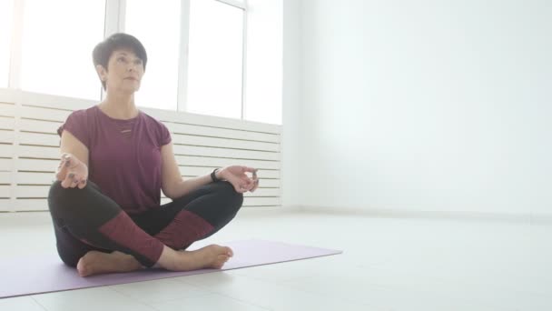 Uyum, spor ve sağlık kavramı. Orta yaşlı bir kadın beyaz bir iç yoga yapıyor — Stok video