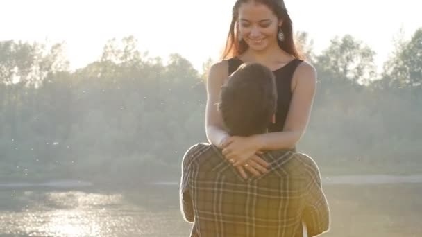 Concept of love and relationships. Young couple hugging at sunset by the river — Stock Video