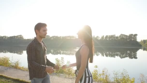 Aşk ve ilişkiler kavramı. Genç çift günbatımında nehir kenarında sarılma — Stok video