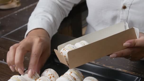 Concept van kleine bedrijven en zoetwaren. Banketbakkers handen zet macarons in een doos — Stockvideo
