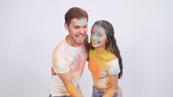 Jovem casal se divertindo com tintas holi em um fundo branco — Vídeo de Stock