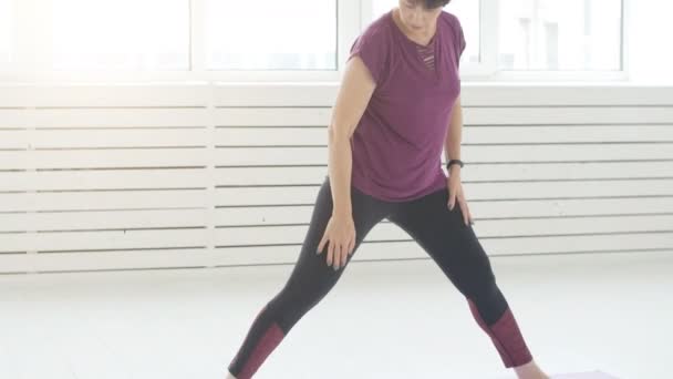 Жінка середнього віку робить йогу в білому інтер'єрі вдома — стокове відео