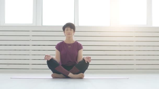 Medelålders kvinna gör yoga i vit inredning hemma — Stockvideo