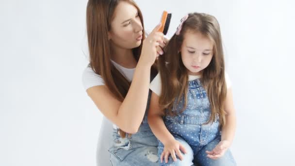 Щаслива мати чистить її милі дочки волосся на білому інтер'єрі — стокове відео
