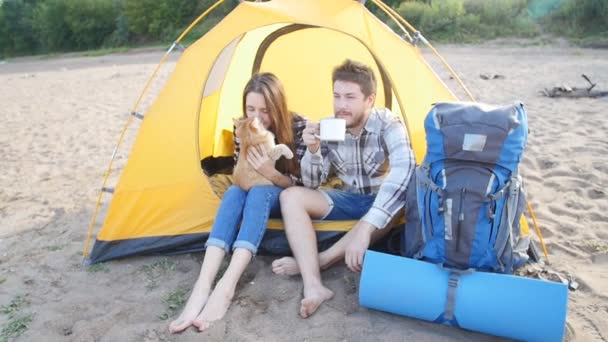 junges glückliches Paar mit Katze sitzt bei Wanderausflug im Zelt