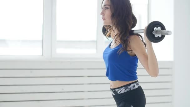 Fitness, deporte, entrenamiento y concepto de estilo de vida - Mujer joven con los músculos de flexión de la barra en el gimnasio interior blanco — Vídeo de stock