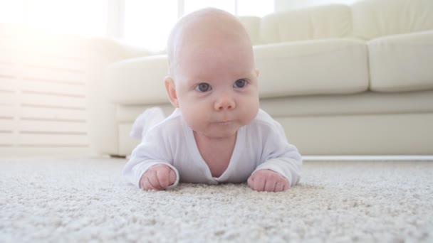 Lindo bebé divertido acostado en una alfombra beige — Vídeos de Stock