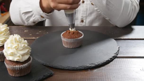 Бейкер прикрашає смачний кекс вершками за столом. Концепція харчових і кондитерських виробів — стокове відео