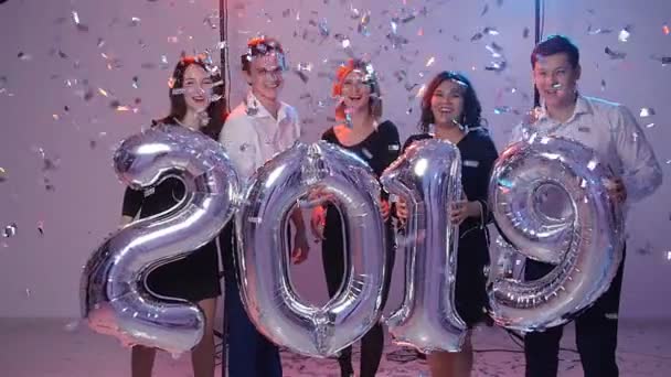 Año nuevo 2019 concepto. Grupo de jóvenes alegres sosteniendo globos numéricos, bañados con confeti — Vídeo de stock