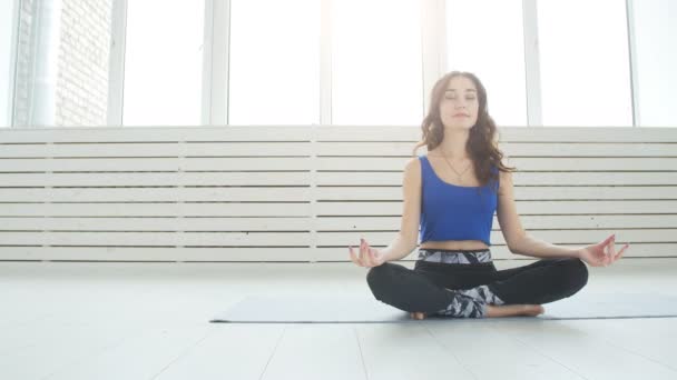 Концепция йоги и домашних тренировок. Молодая женщина медитирует во время занятий йогой в помещении — стоковое видео