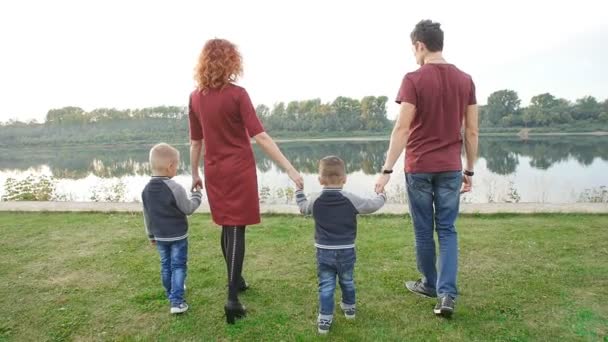 Concepto de familia e hijos. Pareja joven con dos hijos caminando junto al río — Vídeos de Stock