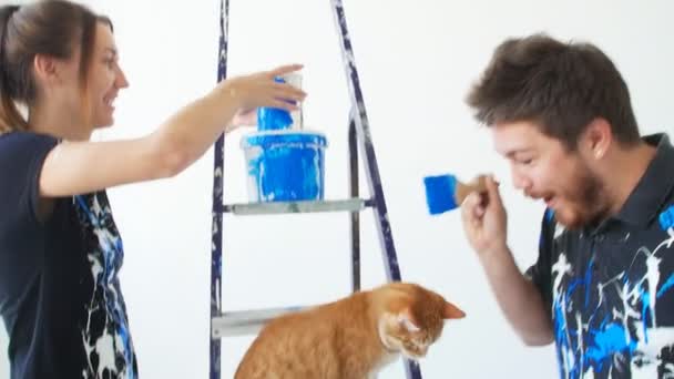 Η έννοια των νέων ακινήτων. Νεαρό ζευγάρι με γάτα ζωγραφική και ανακαίνιση ένα δωμάτιο στο νέο σπίτι τους — Αρχείο Βίντεο