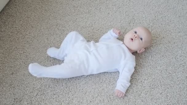 幸せな赤ちゃんは仰向けカーペット バック グラウンド 屋内で白服幼児子供の笑顔の女の子 — ストック動画