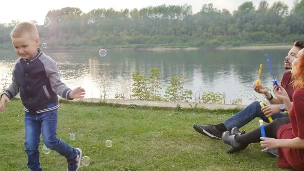 Concepto de amor y paternidad. Familia feliz con los niños soplar burbujas de jabón al aire libre — Vídeo de stock