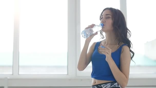 Giovane donna sta bevendo acqua dopo l'allenamento sull'interno bianco — Video Stock