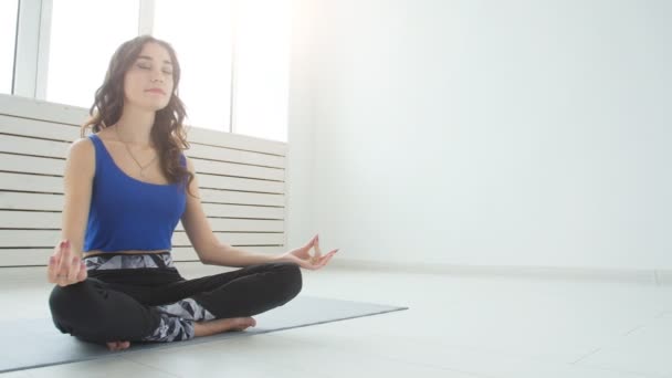 Sportig ung kvinna utövar yoga, sitter i Half Lotus motion, Siddhasana pose, inomhus, hem interiör bakgrund — Stockvideo