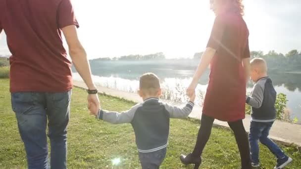 Feliz familia joven con dos hijos camina y descansa en un parque junto al río. Concepto de familia y relación — Vídeos de Stock