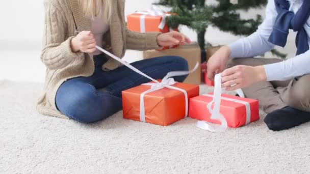 Junges glückliches Paar öffnet Weihnachtsgeschenke in einem Raum mit weißem Interieur. — Stockvideo
