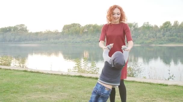 Familie en kinderen concept. Jonge moeder met zoon wandelen door de rivier — Stockvideo