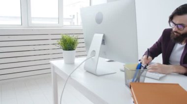 Ofis işleri veya freelancing kavramı. Şık adam ofiste bilgisayarda çalışan genç sakallı