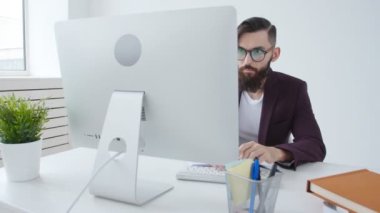 Ofis işleri veya freelancing kavramı. Şık adam ofiste bilgisayarda çalışan genç sakallı