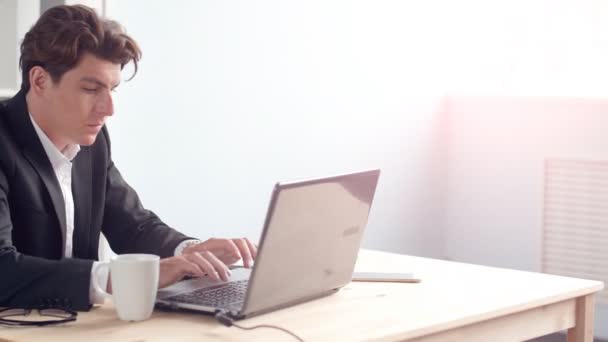 Jeune homme assis à son bureau dans le bureau ensoleillé — Video