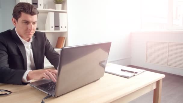 Junger Mann sitzt an seinem Schreibtisch im sonnigen Büro — Stockvideo