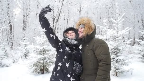 Conceito de viagem de inverno. Jovem casal feliz fazendo foto selfie no smartphone ao ar livre com floresta de neve no fundo — Vídeo de Stock