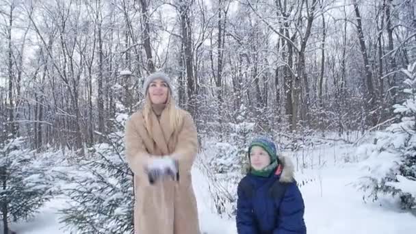 Diversión invernal. Feliz madre e hijo lanzando nieve en el aire en el bosque o parque de invierno — Vídeo de stock