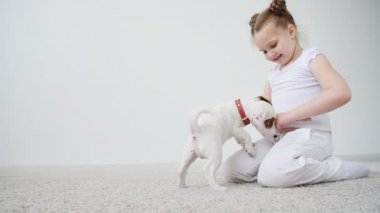 Küçük kızla evde beyaz iç mindere oynayan köpek