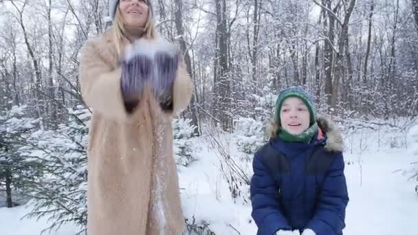 Winterspaß. glückliche Mutter und Sohn, die im Winterwald oder Park Schnee in die Luft werfen — Stockvideo