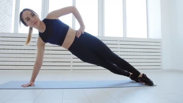Concepto de deporte y fitness en el hogar. Mujer joven haciendo ejercicios de fitness en un interior blanco — Vídeos de Stock