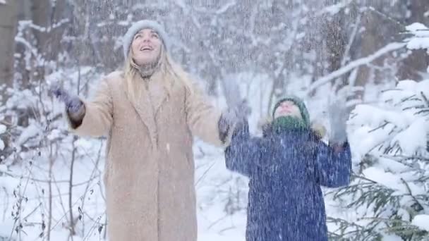 Diversão de inverno. Mãe e filho felizes jogando neve no ar na floresta ou parque de inverno — Vídeo de Stock