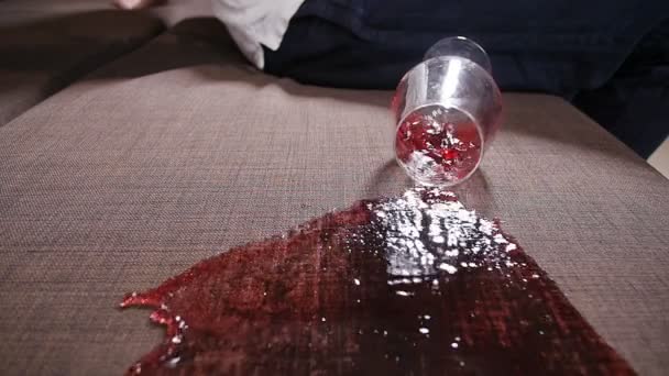 Een glas wijn valt op de sofa en morst wijn. — Stockvideo