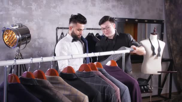 Seller in the costume shop helps the young man to choose a suit — Stock Video