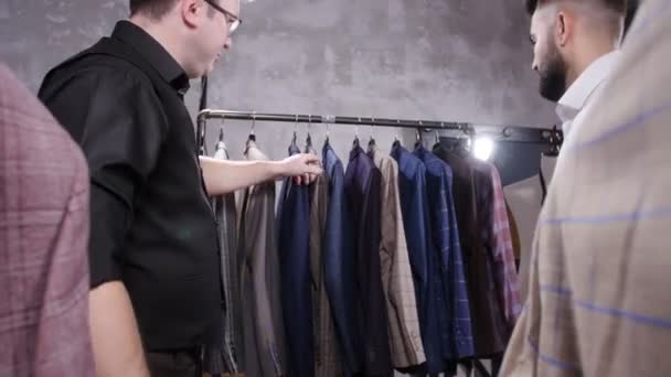 Satıcı kostüm dükkanında genç adam bir takım elbise seçmek için yardımcı olur. — Stok video