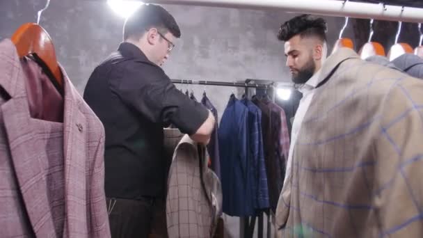 Vendeur dans la boutique de costumes aide le jeune homme à choisir un costume — Video