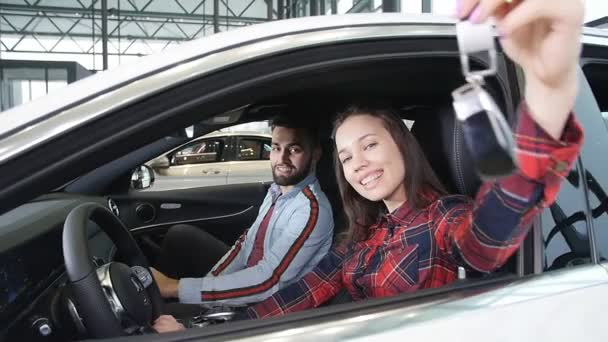 Um jovem casal feliz compra um carro novo. Sorri e mostra as chaves — Vídeo de Stock