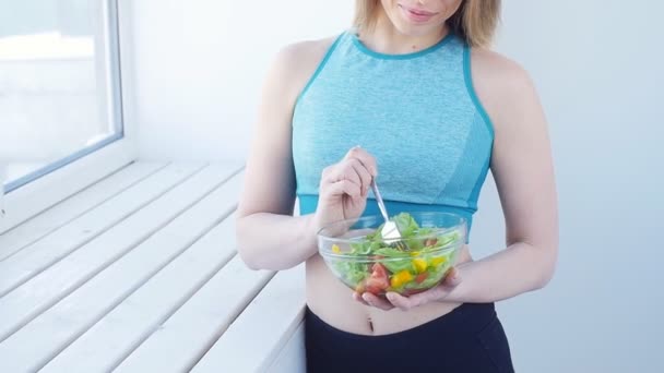 Conceito de alimentação saudável. Mulher feliz comendo salada verde saudável após o treino em um interior branco — Vídeo de Stock