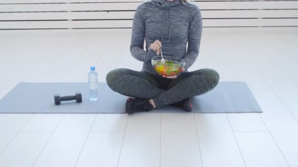 健康食品のコンセプトです。白のインテリアでのトレーニングの後健康的なグリーン サラダを食べて幸せな女 — ストック動画