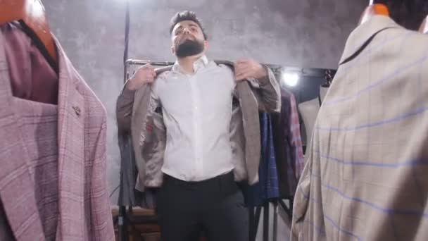 Alışveriş ve moda konsepti - Alışveriş merkezinde veya giyim mağazasında ceketi seçen ve deneyen genç sakallı adam — Stok video