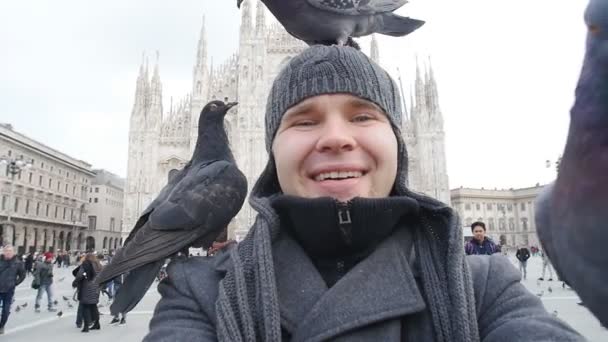 Viajes, vacaciones y vacaciones de invierno concepto - Feliz joven tomar foto selfie con palomas divertidas en frente de la Catedral de Milán Duomo — Vídeos de Stock